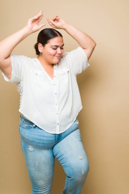Beautiful fat hispanic woman dancing with music and having fun with body positivity against a studio background 