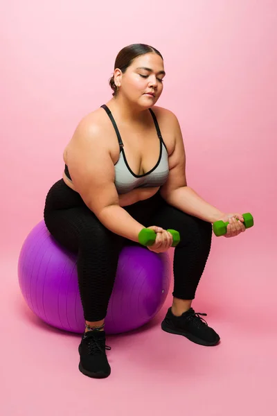 Big Young Woman Using Fitness Ball Lifting Dumbbell Weights While — Stockfoto