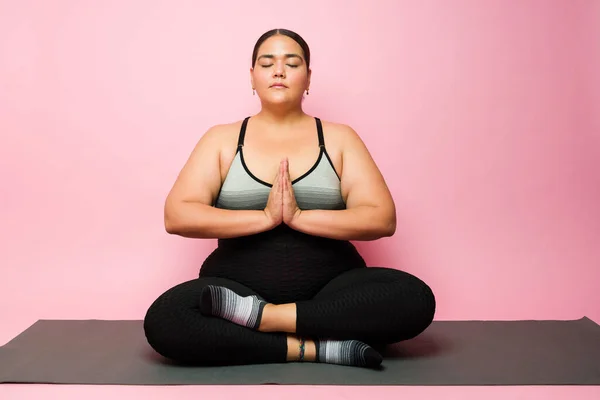Relaxed fat woman on a prayer pose doing a yoga workout and relaxing with a meditation on an exercise mat