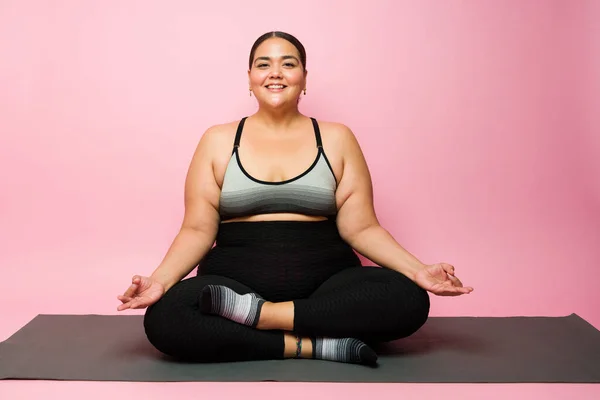 Portrait of a happy obese woman smiling and making eye contact while ready to do a yoga workout on an exercise mat