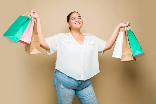 Beautiful fat woman laughing and looking happy after buying in the mall and holding her shopping bags against a yellow background