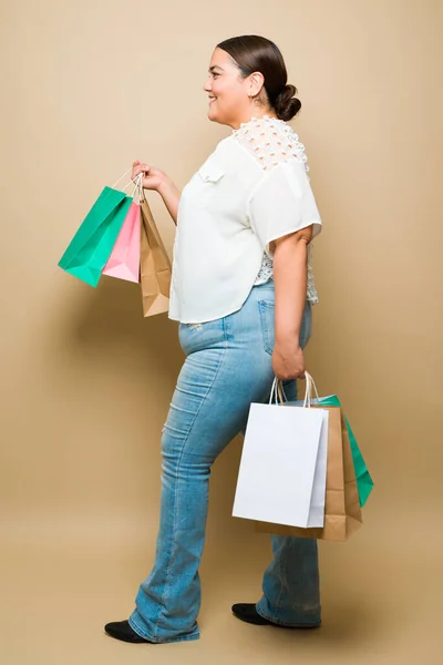Profile of an overweight woman walking in the mall and holding her shopping bags against a yellow background