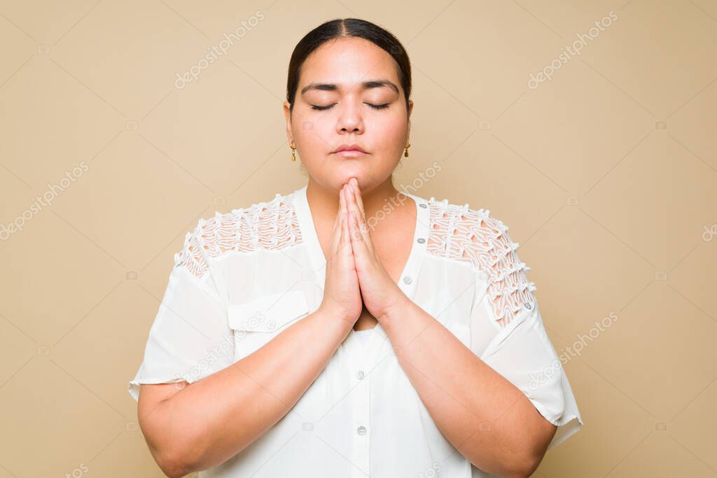 Faithful plus size woman praying or meditating while looking relaxed against a yellow background