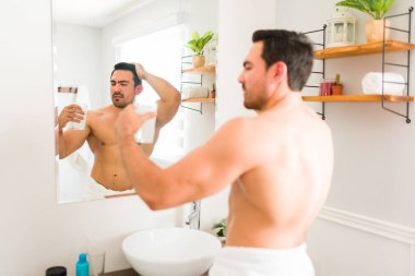 Stressed young man looking worried while taking a drink with vitamins or collagen while grooming and getting ready