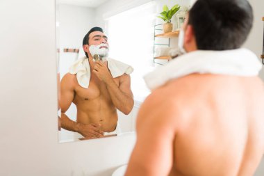 Athletic young latin man using shaving cream in his beard with a brush before shaving and grooming