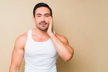 Studio shot of a happy caucasian man wearing an undershirt and touching his face after using skin care products