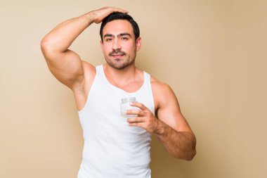 Smiling handsome muscular man in an undershirt doing a hairstyle and putting hair gel against a studio background