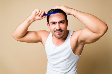 Cheerful caucasian young man smiling while combing his hair and grooming against a yellow studio background