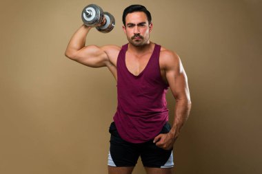 Athletic hispanic man exercising lifting dumbbell weights during his fitness workout against a studio background