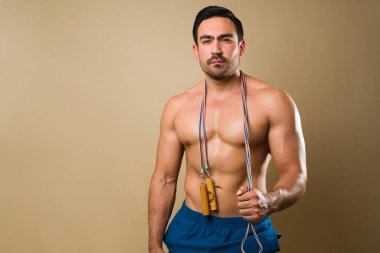 Portrait of a shirtless latin man using a jump rope during his cardio workout standing in front of a yellow background with copy space