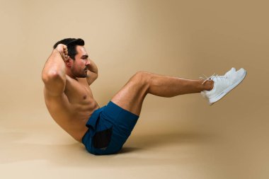 Side view of a strong hispanic young man with strong abs doing sit ups and abdominal crunches while exercising