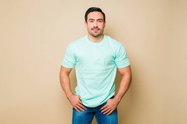 Happy handsome latin man smiling wearing a blue casual t-shirt and jeans while standing in front of a yellow background