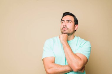 Thoughtful young man thinking about a new smart idea while using his imagination with a hand on his chin against a studio background with copy space
