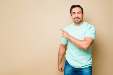 Cheerful attractive man smiling pointing with his finger to an ad copy space against a yellow background