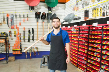 Happy hardware store retail worker holding a shovel in the construction sector of the hardware store