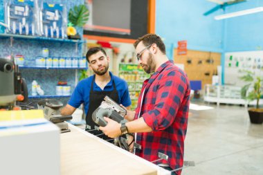 Attractive man customer or carpenter looking to buy a power tool or polisher while taking with the hardware store worker