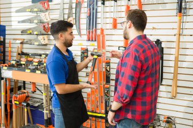 Male customer asking for help to a hardware shop worker to buy a new hammer and construction tools