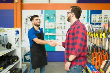 Cheerful male employee smiling shaking hands with a young man and greeting him to the hardware store during his shopping