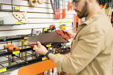 Close up of a young man and customer looking at the tools at the hardware store and buying a new saw