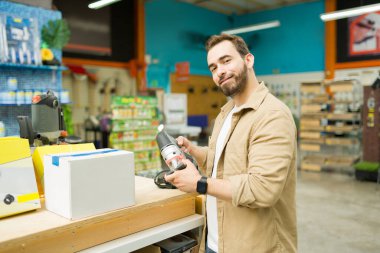 Cheerful attractive smiling customer looking at the camera while buying power tools at the hardware store