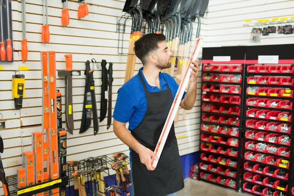 Handsome hardware store worker looking at a level tool and working in the construction tools aisle at the shop