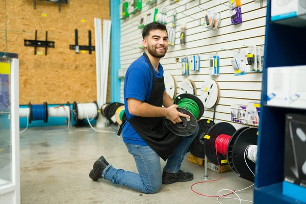 Attractive happy young man working as a hardware store worker and feeling happy while looking for electricity cable