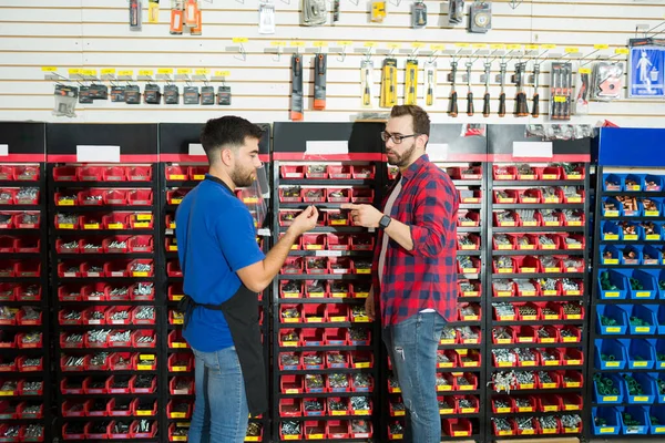 Hardware store worker showing different screws to a young man client looking to buy tools