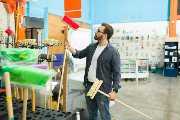 Attractive male customer at the hardware store choosing which broom to buy while shopping