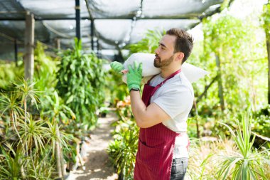 Side view of a young man working at the nursery garden and carrying fertilizer soil for the new trees 