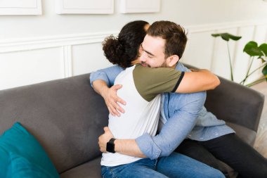 Rear view of a cute gay couple hugging and feeling in love while sharing a romantic moment while relaxing on the couch at home