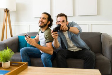 Excited gay couple having fun playing video games and laughing together while hanging out in the living room