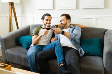 Attractive man and his partner cuddling having a glass of wine while hanging out in the living room