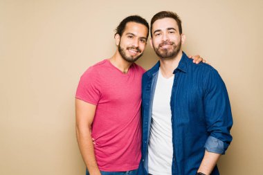 Studio portrait of an attractive happy gay couple hugging wearing casual clothes against a pastel background