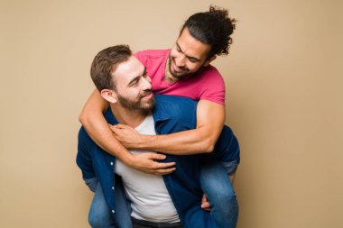 Cheerful attractive gay man and his partner laughing and having fun while piggybacking 