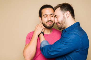 Relaxed romantic gay couple embracing closing their eyes and sharing a passionate moment together