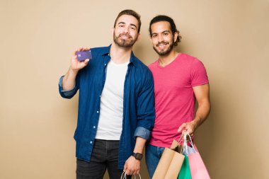 Attractive queer couple carrying their gift bags and paying for their shopping at the mall with a credit card 
