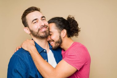 Adorable gay man smiling while hugging his attractive partner during a romantic moment against a yellow background