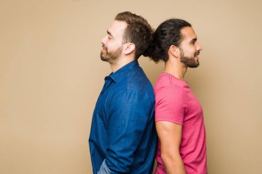 Side view of an attractive happy gay couple standing back to back and smiling against a yellow studio background