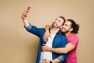 Cheerful caucasian gay man taking a selfie using a smartphone with his smiling happy partner to post on social media