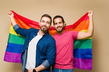 Confident gay multiracial men looking happy holding a rainbow flag to support LGBT rights in front of a studio background