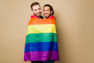 Excited attractive gay couple laughing while playing with a rainbow flag during a LGBT parade