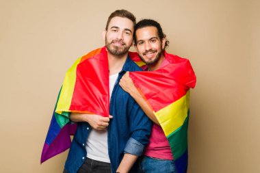 Portrait of an attractive queer couple using a rainbow flag while hugging and supporting the gay LGBT community