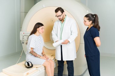Male doctor and nurse showing the exam results to a female patient sitting on the MRI machine at the medical imaging center