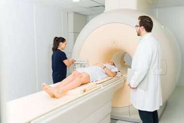 Female patient getting a medical test at the hospital and doing a magnetic resonance to check for cancer with a doctor and radiologist