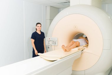 Beautiful radiologist technician smiling and looking happy while doing a magnetic resonance on the brain of a female patient