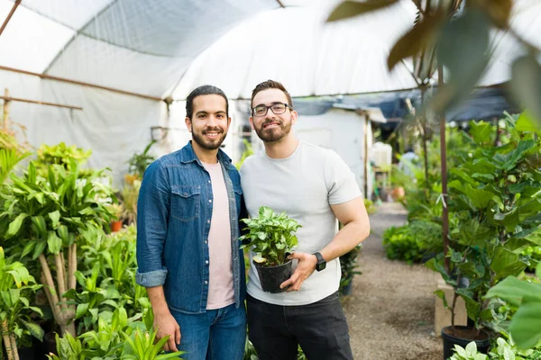 Handsome gay couple with a gardening hobby at the nursery garden smiling while buying new plants together