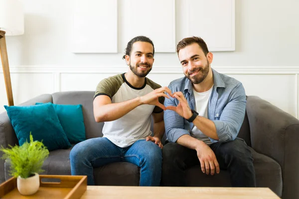 Handsome attractive couple feeling in love making a heart gesture with their hands together while resting in the living room