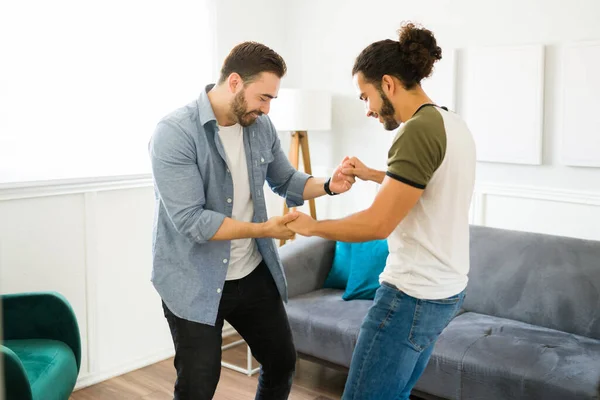 Fun young gay couple dancing together while listening to dance music in the living room