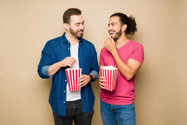 Romantic gay couple eating popcorn and laughing while watching a movie together during a fun date