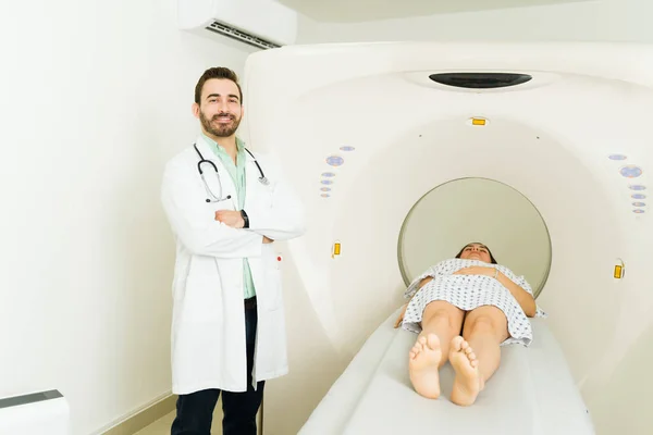 Cheerful doctor wearing a lab coat smiling while doing a cat scan or tomography test on a female patient at the imaging laboratory